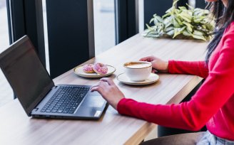 a woman works at a wooden bench on a computer, with coffee & donuts